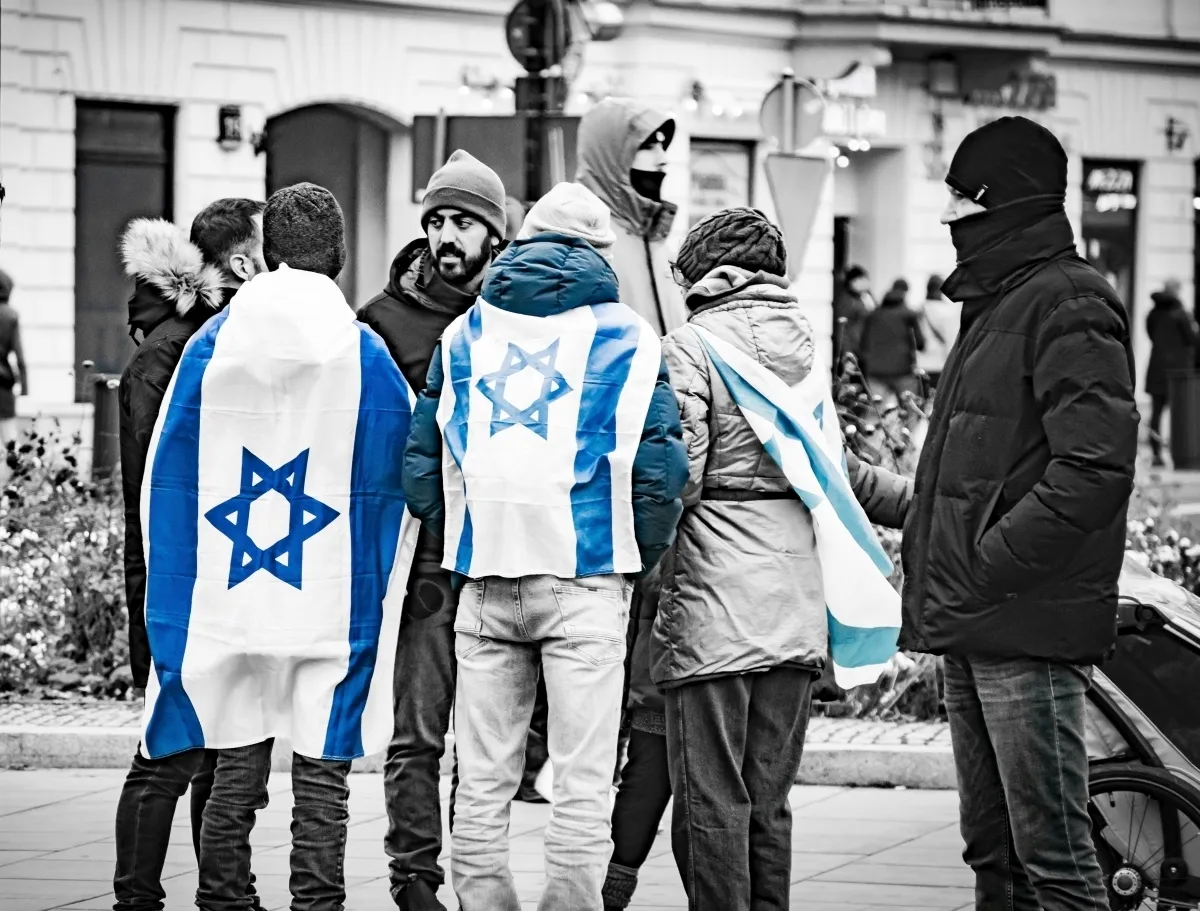 Two people draped in Israeli flags facing a masked protester